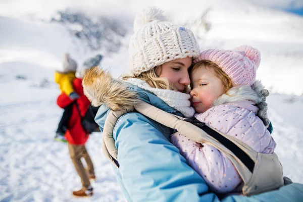 Mor med glad liten dotter i bärare stående i vinternaturen, vila. — Stockfoto