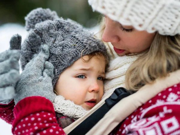 Primer plano de la pequeña hija molesta en el portador y la madre en la naturaleza de invierno. —  Fotos de Stock