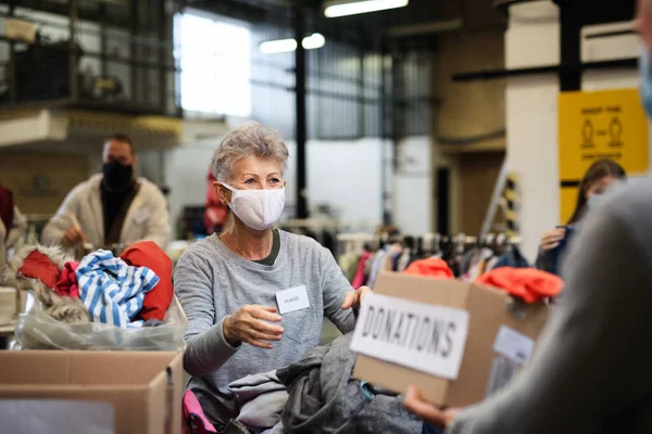 Добровольцы сортируют пожертвованную одежду в общественном благотворительном центре, коронавирусную концепцию. — стоковое фото