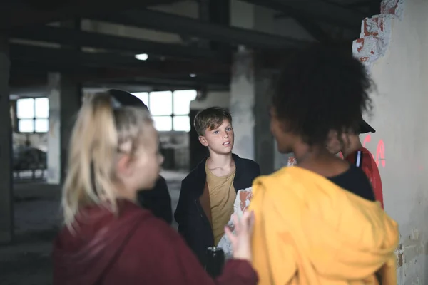 Skupina teenagerů stojí uvnitř v opuštěné budově a mluví. — Stock fotografie