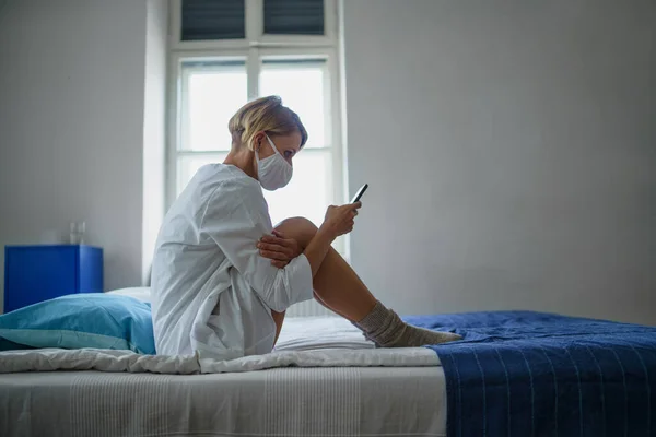 Női beteg okostelefonnal ül az ágyon a kórházban, mentális egészség és a koronavírus koncepció. — Stock Fotó