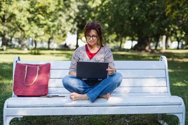 Mature woman with laptop outdoors in city or town park, working. — Stock Photo, Image