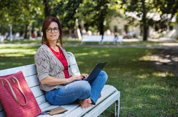 Gammal kvinna med bärbar dator utomhus i staden eller stadsparken, arbetar. — Stockfoto