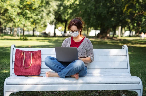 Gammal kvinna arbetar med bärbar dator utomhus i staden eller stadsparken, coronavirus koncept. — Stockfoto
