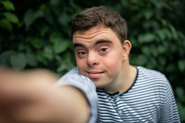 Retrato da síndrome de down homem adulto em pé ao ar livre no jardim, tomando selfie. — Fotografia de Stock