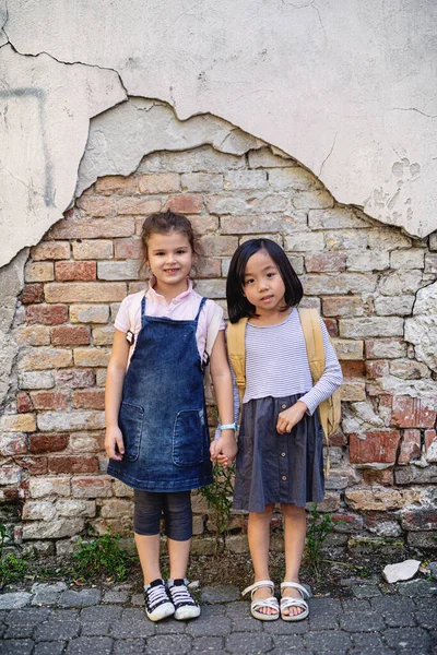 Piccole ragazze che guardano la fotocamera all'aperto in città, in piedi contro il vecchio muro di mattoni. — Foto Stock