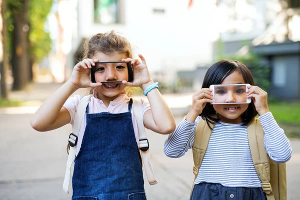 Μικρά κορίτσια κρατώντας smartphone μπροστά από τα μάτια σε εξωτερικούς χώρους στην πόλη. — Φωτογραφία Αρχείου