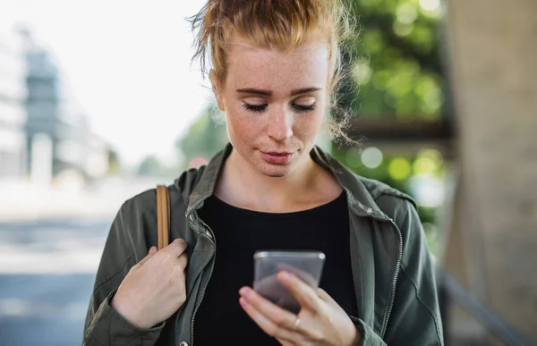 Portrét mladé ženy s rudými vlasy venku ve městě, pomocí smartphonu. — Stock fotografie