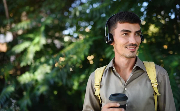 Młody człowiek ze słuchawkami i kawą w kubku wielokrotnego użytku spacerujący po mieście. — Zdjęcie stockowe