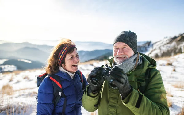 Starší pár turisté pomocí dalekohledu ve zasněžené zimní přírodě. — Stock fotografie