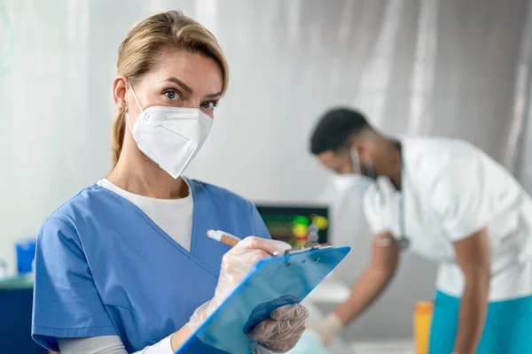 Portret van arts met gezichtsmasker en klembord in ziekenhuis, coronavirus concept. — Stockfoto