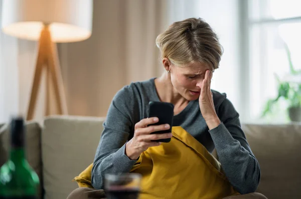 Mulher com smartphone dentro de casa no sofá em casa sentindo-se estressado, conceito de saúde mental. — Fotografia de Stock