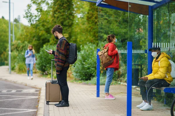 Молодые люди со смартфоном на автобусной остановке в городе. Коронавирусная концепция. — стоковое фото