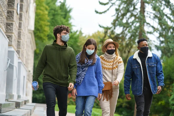 Jovens estudantes com máscara facial ao ar livre por prédio da escola, caminhando. Conceito de coronavírus. — Fotografia de Stock