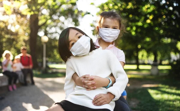 Små skolflickor med ansiktsmask på lekplatsen utomhus i stan, coronavirus koncept. — Stockfoto