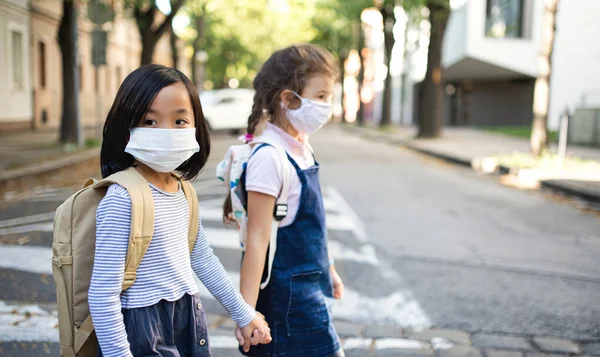 Små skolflickor med ansiktsmask utomhus i stan, coronavirus koncept. — Stockfoto