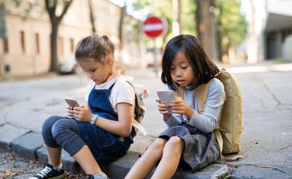Chicas pequeñas con teléfonos inteligentes al aire libre en la ciudad, jugando. — Foto de Stock