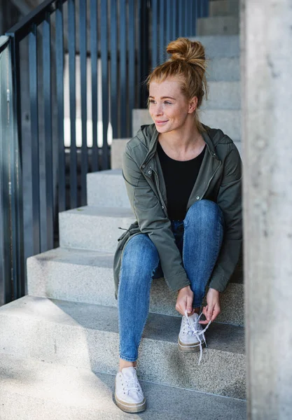 Portrait de jeune femme aux cheveux roux à l'extérieur en ville, attachant des lacets sur l'escalier. — Photo