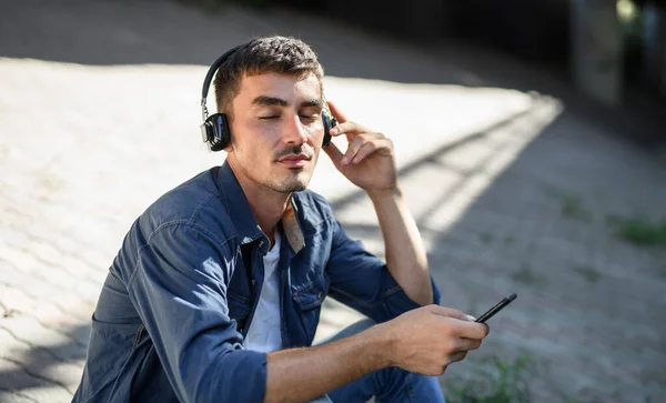 Portret młodego atrakcyjnego mężczyzny ze smartfonem siedzącym na świeżym powietrzu w mieście. — Zdjęcie stockowe