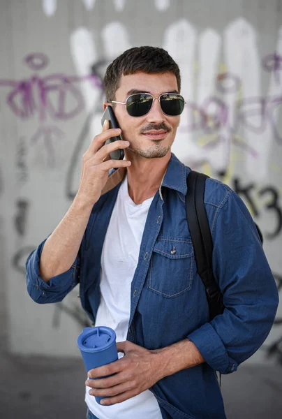 Вид на молодого привлекательного человека со смартфоном, стоящего на улице в городе. — стоковое фото