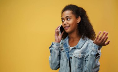 Stüdyoda genç bir kız sarı arka planda, akıllı telefon kullanıyor..