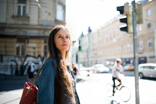 Femme mûre marchant à l'extérieur dans la ville ou le parc municipal, traversant la rue. — Photo