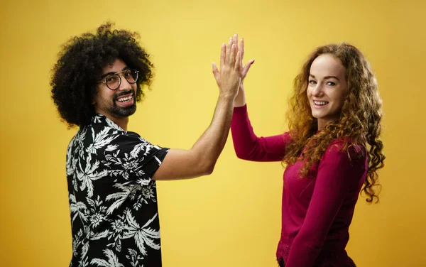 Hombre maduro y mujer joven en un estudio sobre fondo amarillo, dando alta cinco. — Foto de Stock