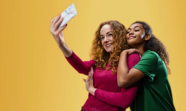 Mujer joven con chica adolescente en un estudio sobre fondo amarillo, tomando selfie. — Foto de Stock