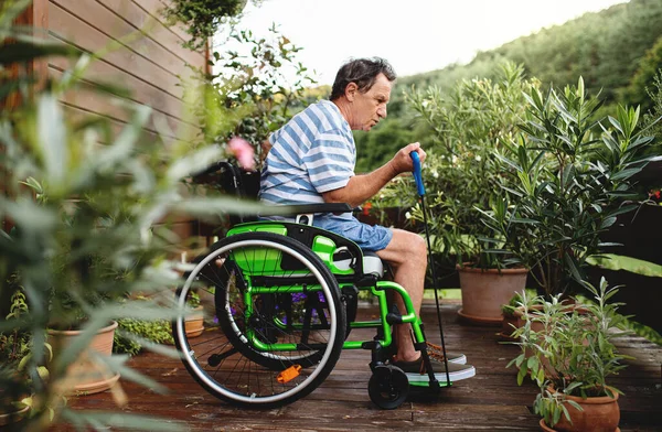 Senior na wózku inwalidzkim ćwiczy na tarasie. — Zdjęcie stockowe