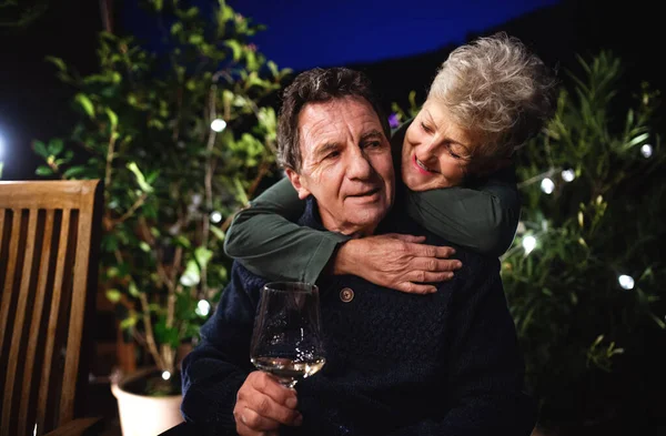 Senior couple with wine in the evening on terrace, hugging. — Stock Photo, Image