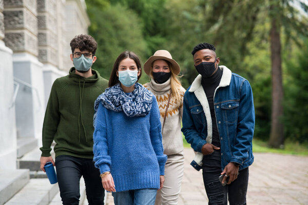 Group of young people with face mask outdoors in town, walking. Coronavirus concept.