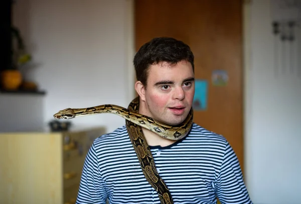 Síndrome de Down homem adulto sentado em casa no quarto, brincando com cobra de estimação. — Fotografia de Stock