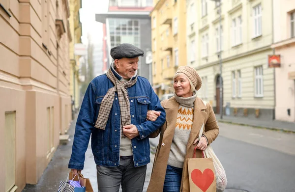 Feliz casal sênior andando ao ar livre na rua na cidade, levando sacos de compras. — Fotografia de Stock