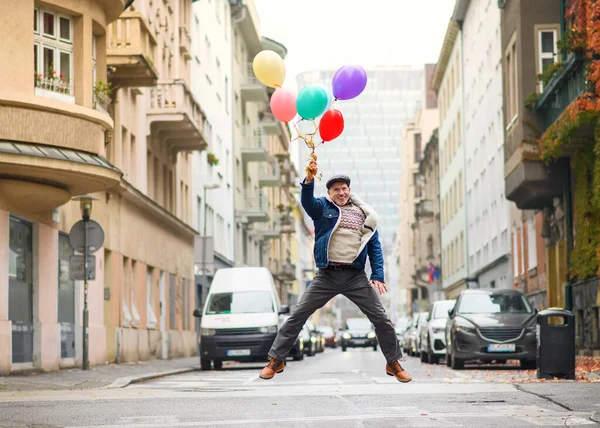 Szczęśliwy senior z balonami na świeżym powietrzu na ulicy w mieście, skoków. — Zdjęcie stockowe