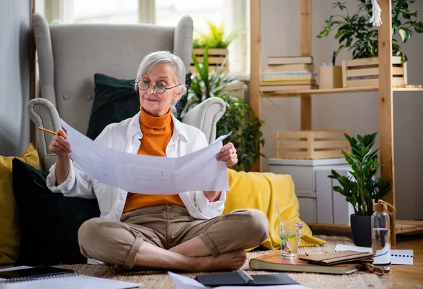 Portret van een oudere vrouwelijke architect die thuis op de vloer zit en werkt. — Stockfoto