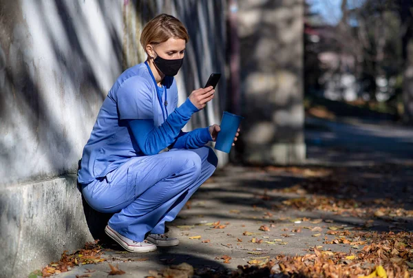 Žena pečovatel nebo zdravotnický pracovník s smartphone venku na cestě do práce, koronavirus koncept. — Stock fotografie