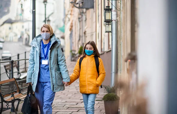 Женщина медицинский работник на открытом воздухе на пути к работе со школьницей дочь, коронавирус концепции. — стоковое фото