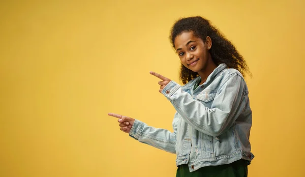 Small girl in a studio on yellow background, pointing fingers at copy space. — Stock Photo, Image