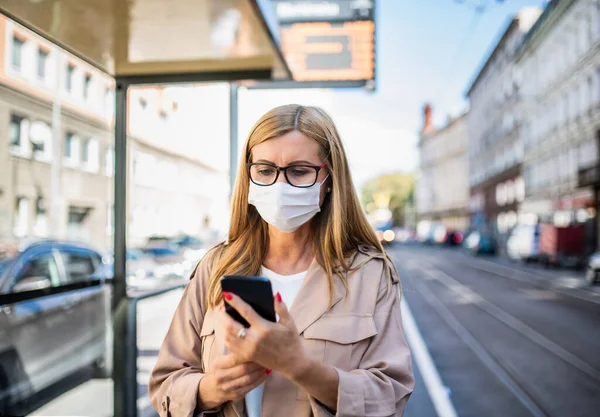 Ανώτερη γυναίκα με smartphone σε στάση λεωφορείου σε εξωτερικούς χώρους στην πόλη ή την πόλη, έννοια coronavirus. — Φωτογραφία Αρχείου