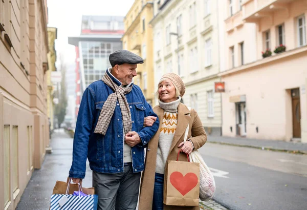 Счастливая пожилая пара, гуляющая на улице по городу, с сумками для покупок. — стоковое фото