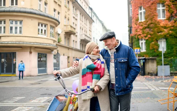 Heureux couple de personnes âgées avec vélo marchant à l'extérieur dans la rue en ville, portant des sacs à provisions. — Photo