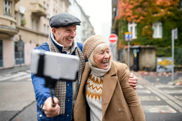 Šťastný starší pár procházky venku na ulici ve městě, přičemž selfie. — Stock fotografie