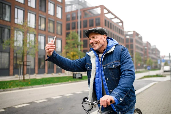 Heureux homme âgé avec vélo à l'extérieur dans la rue en ville, en prenant selfie. — Photo