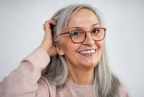 Porträt einer Seniorin, die drinnen vor hellem Hintergrund steht und in die Kamera blickt. — Stockfoto