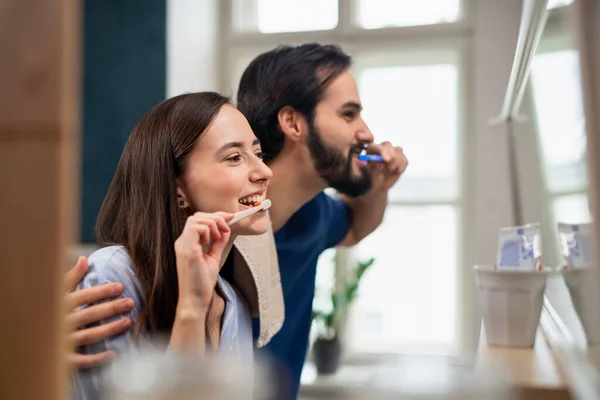 Pareja joven cepillándose los dientes delante del espejo en casa. —  Fotos de Stock