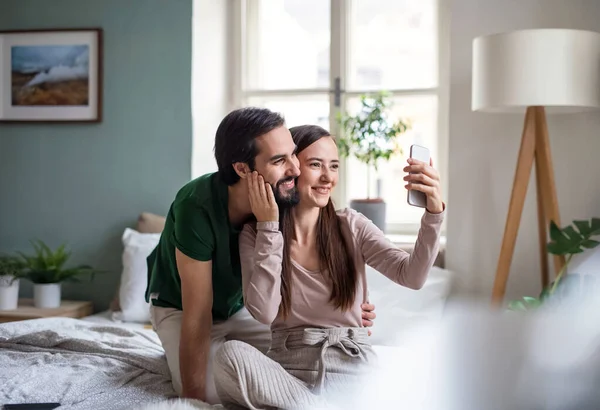 Νεαρό ζευγάρι ερωτευμένο να βγάζει selfie στο κρεβάτι στο σπίτι. — Φωτογραφία Αρχείου