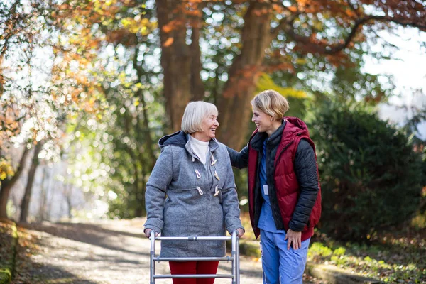 Seniorin mit Gehgestell und Pflegerin auf Spaziergang im Park, Coronavirus-Konzept. — Stockfoto