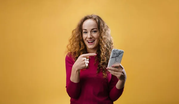 Stüdyoda sarı arka planda genç bir kadının portresi akıllı telefonu işaret ediyor.. — Stok fotoğraf