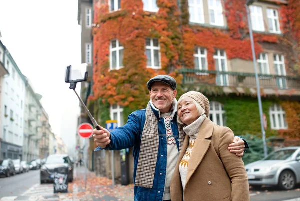 Casal sênior feliz andando ao ar livre na rua na cidade, tomando selfie. — Fotografia de Stock