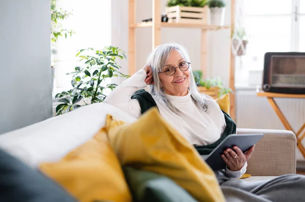 Portret van oudere vrouw die thuis op de bank zit, met behulp van een tablet. — Stockfoto